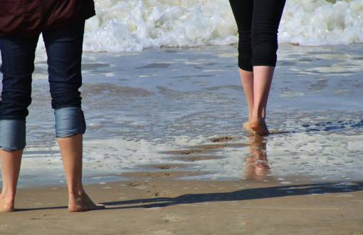 Zwei Personen laufen mit hochgekrempelten Hosen und barfuß ins Meer beim Kneippen im Urlaub in den Arkona Strandresidenzen.