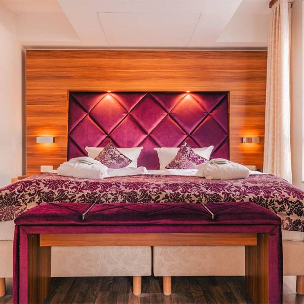 Doppelbett im Suite Apartment der Arkona Strandresidenzen Binz mit dekorativen Kissen und Tagesdecke in Lila