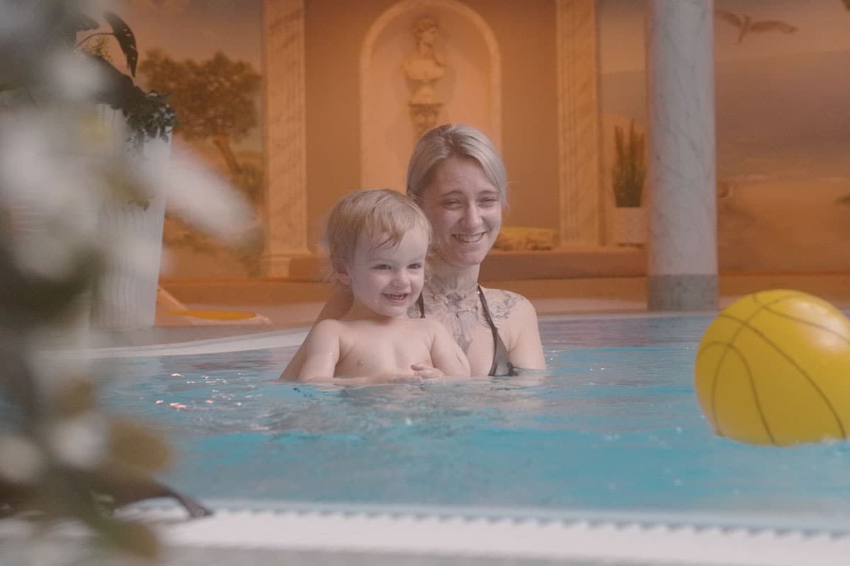 Mutter und Kind spielen mit einem gelben Wasserball im Hotelpool des Arkona Strandhotels